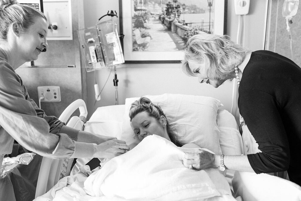 mom, grandma, and nurse looking at newborn baby boy 