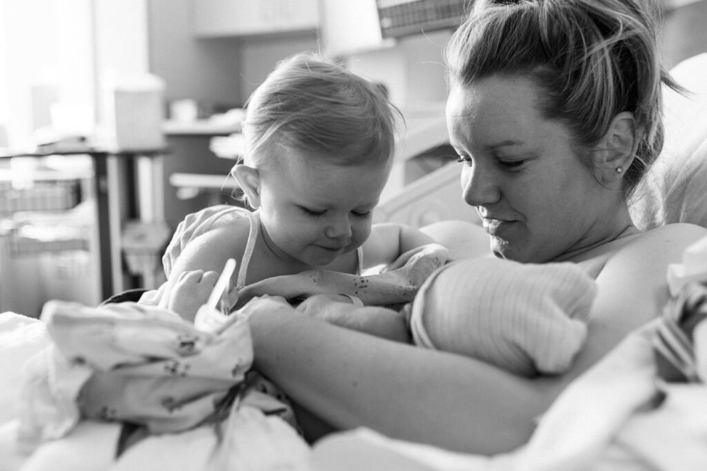 mom and daughter looking at newborn son in hospital