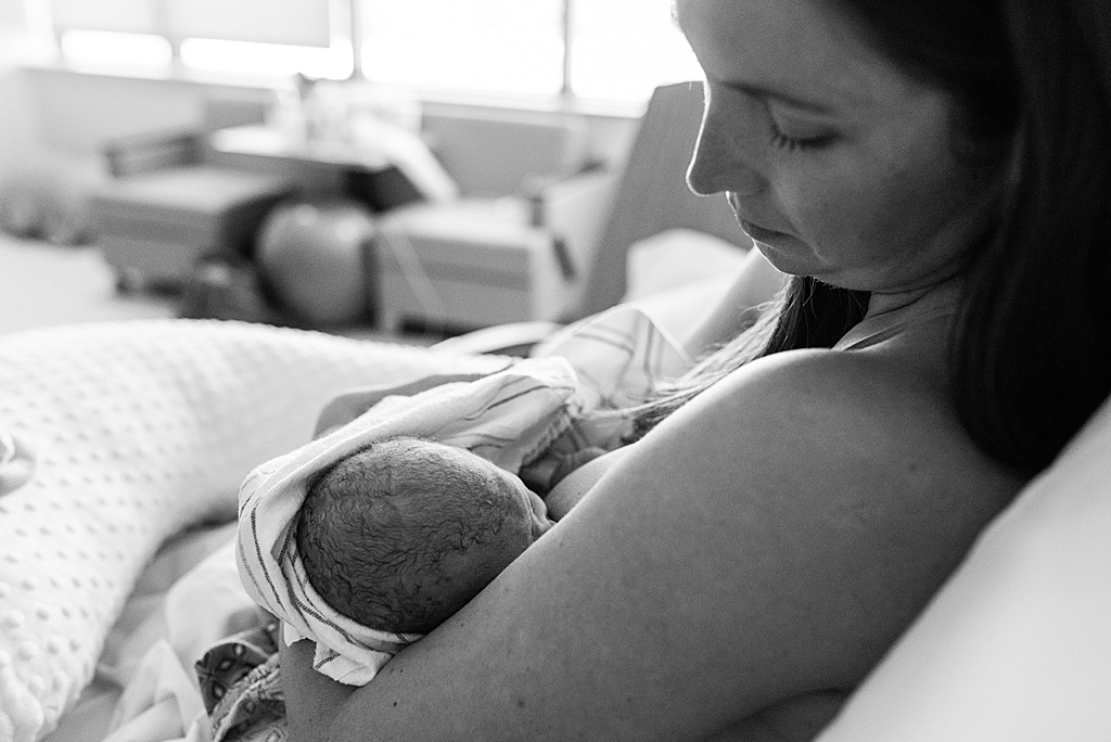 mom breastfeeding newborn in hospital bed